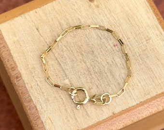 May include: A gold chain bracelet with a lobster clasp closure. The bracelet is on a wooden surface.