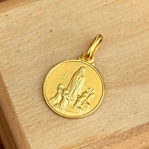 May include: A gold-coloured pendant featuring a religious image of the Virgin Mary with children. The pendant is round and has a loop at the top for attaching to a chain.