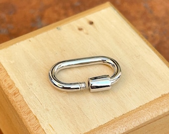 May include: A silver oval-shaped clasp with a screw closure. The clasp is on a light brown wooden surface.