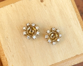 May include: A pair of gold stud earrings with a flower design. Each earring has a small circle in the center surrounded by a ring of small diamonds.