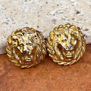 May include: A pair of gold-tone lion head stud earrings. The lion heads are detailed and have a textured finish.
