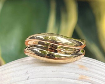 May include: A gold-toned ring with a wavy, double-band design. The ring is sitting on a white seashell.