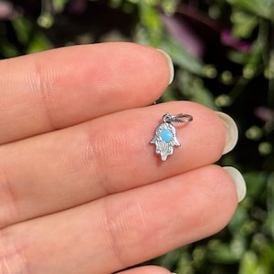 Könnte beinhalten: Ein silberner Anhänger in Form einer Hamsa-Hand mit einem blauen Türkis-Stein in der Mitte.