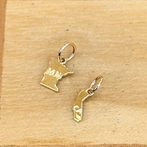 May include: Two gold state charm pendants, one shaped like Minnesota with "MN" engraved on it, and the other shaped like California.