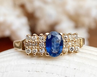 Op de afbeelding: Een gouden ring met een blauwe ovale saffier omringd door kleine diamanten.