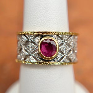 May include: A gold and silver ring with a red ruby gemstone surrounded by smaller diamonds. The ring has a delicate, intricate design.