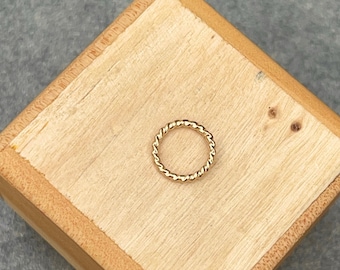 May include: A gold-colored twisted ring on a wooden surface.