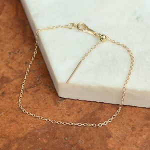 May include: A gold chain bracelet with a sliding clasp and a small ball at the end of the chain.