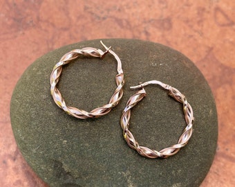 May include: A pair of gold hoop earrings with a twisted design. The earrings are on a gray stone background.