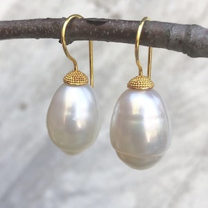 May include: A pair of elegant drop earrings featuring large, lustrous white teardrop-shaped pearls. The pearls are suspended from gold-colored hooks with textured, gold-colored caps, creating a classic and sophisticated look.