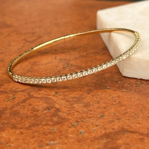 May include: A gold bangle bracelet with a single row of small, clear diamonds.