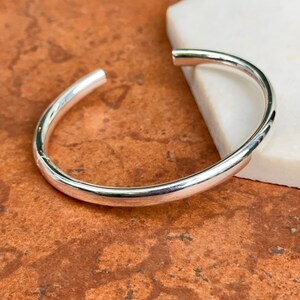 May include: A simple silver bangle bracelet with a smooth, rounded surface.