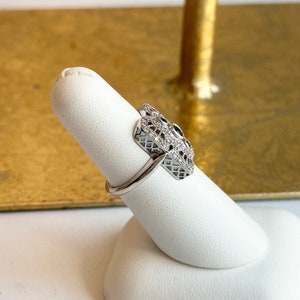 May include: A silver ring with a geometric design set with small clear and black stones.