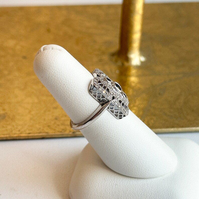 May include: A silver ring with a geometric design set with small clear and black stones.