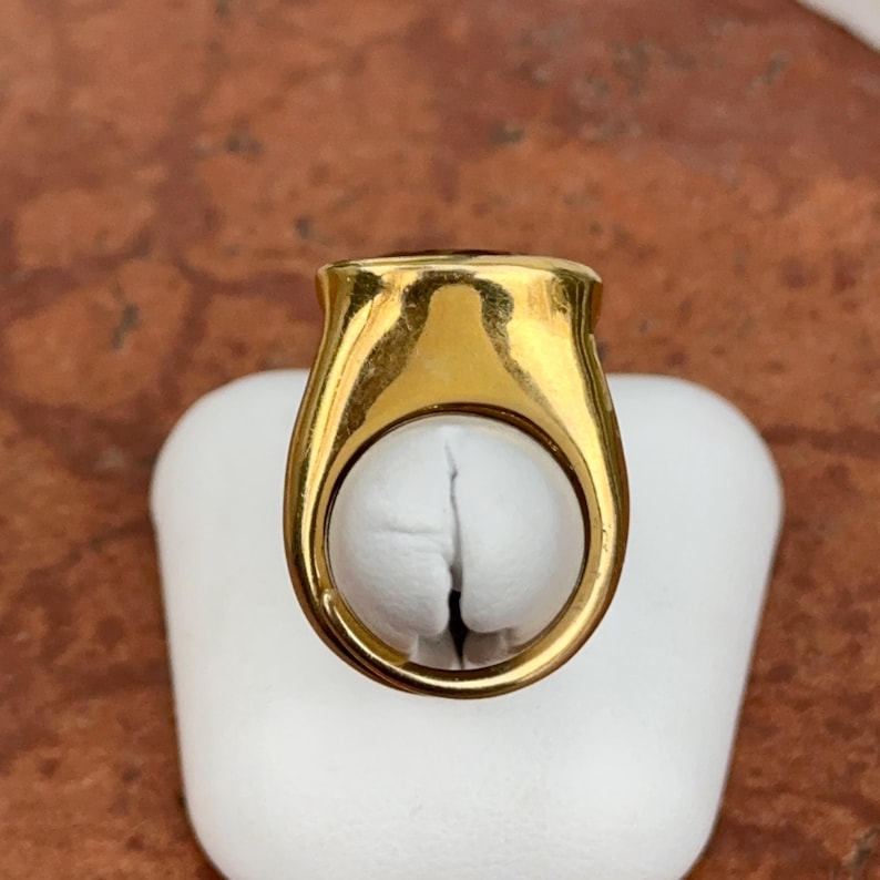 May include: A gold ring with a large, round, dark gemstone. The ring is on a white display stand.