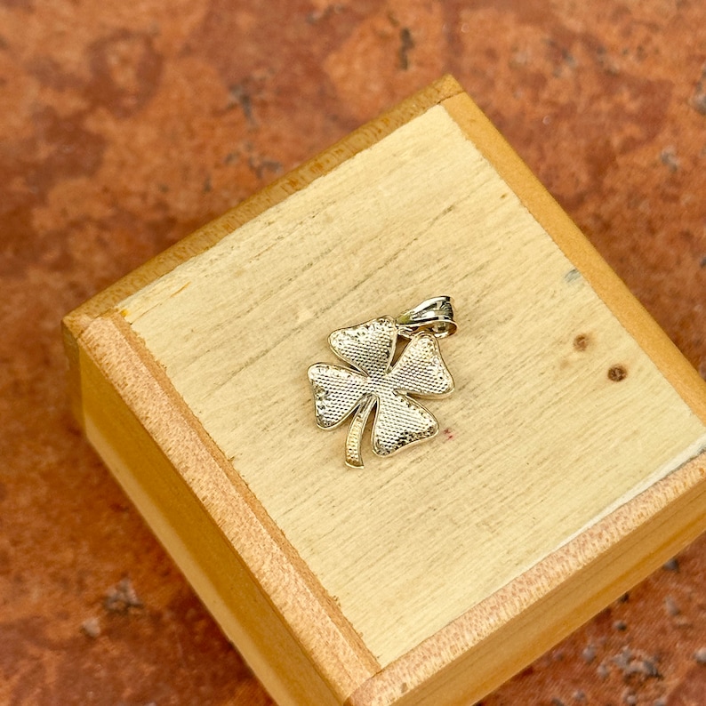 May include: A gold four-leaf clover charm pendant. The pendant is detailed with a textured surface.