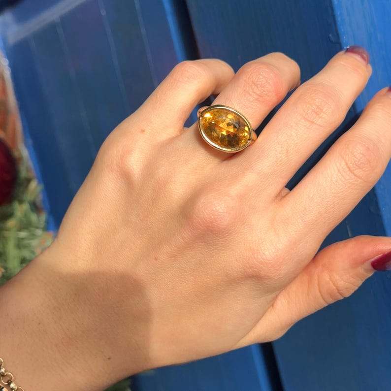 May include: A gold ring with a large, oval-shaped, yellow gemstone.