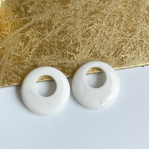May include: Two white ceramic donut-shaped rings with a hole in the center. The rings are smooth and glossy.