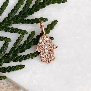 Könnte beinhalten: Ein Hamsa-Anhänger aus Roségold mit einer Pavé-Fassung aus klaren Zirkonia-Steinen.