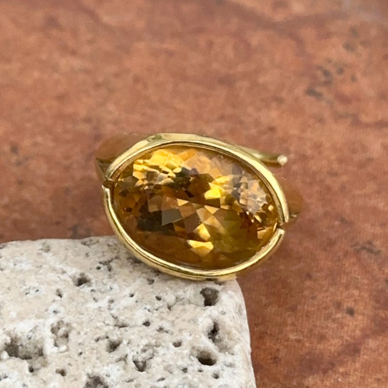 May include: A gold ring with a large, oval-shaped, yellow citrine gemstone.