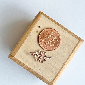 May include: A gold-toned four-leaf clover charm on a wooden surface next to a US penny.