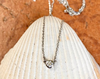May include: A delicate silver chain necklace with a single, round, clear diamond pendant.