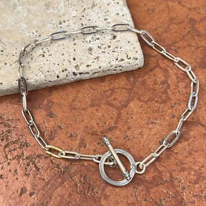 May include: A silver chain bracelet with a toggle clasp. The chain is made of oval links and the clasp is round with a decorative design.