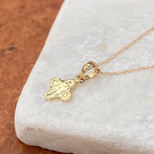 Op de afbeelding: Een gouden ketting met een klein, gedetailleerd kruisje als hanger. Het kruis heeft een getextureerd oppervlak en is een populair religieus symbool.