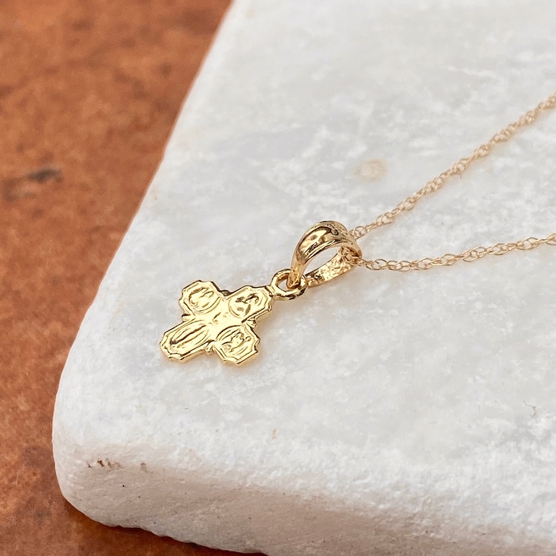 Op de afbeelding: Een gouden ketting met een klein, gedetailleerd kruisje als hanger. Het kruis heeft een getextureerd oppervlak en is een populair religieus symbool.
