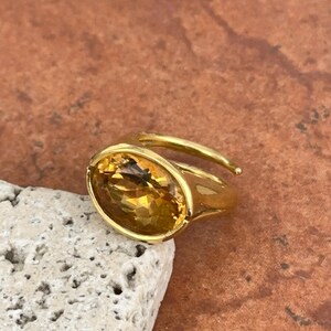 May include: A gold ring with a large, oval-shaped, yellow citrine gemstone.