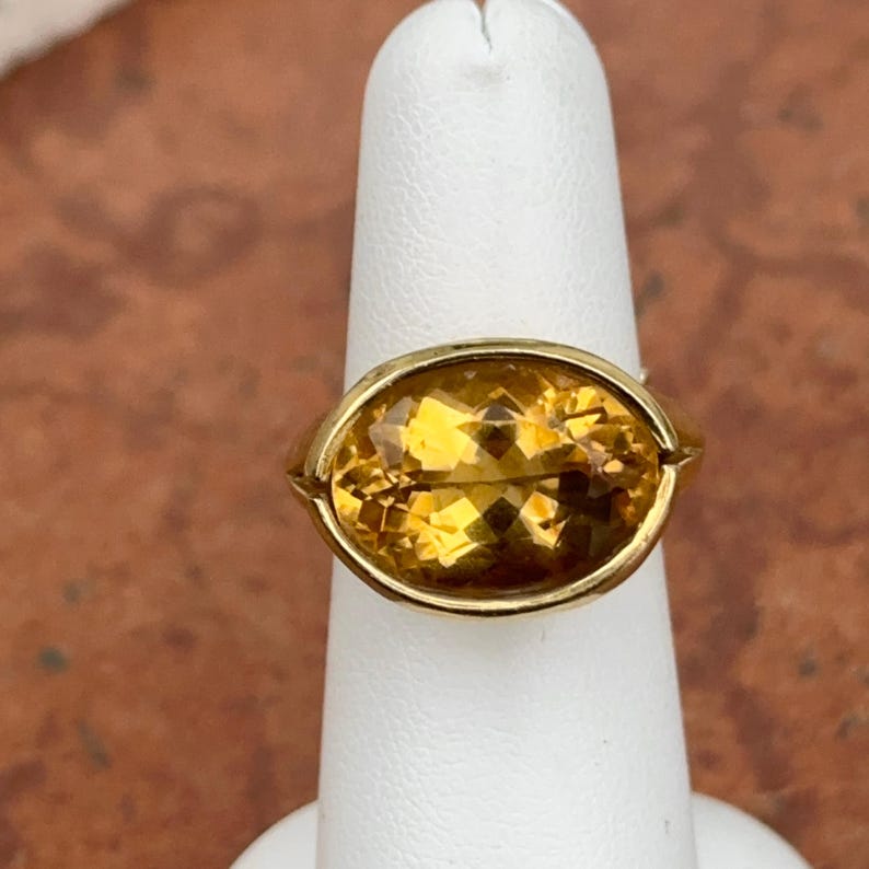 May include: A gold ring with a large, oval-shaped, yellow citrine gemstone.