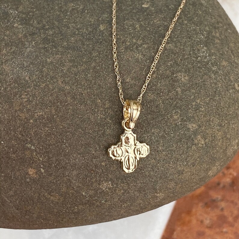 Op de afbeelding: Een gouden ketting met een klein, gedetailleerd kruisje als hanger.