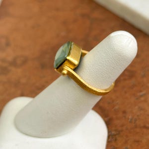 May include: A gold ring featuring a square, light green gemstone. The ring has a textured band and a simple, elegant design. The gemstone is set in a gold bezel.