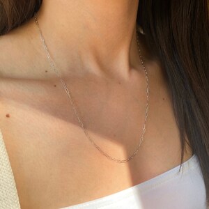 Pu&ograve; includere: Una collana a catena d'argento con un design delicato e collegato. La catena &egrave; indossata da una persona con una camicia bianca.