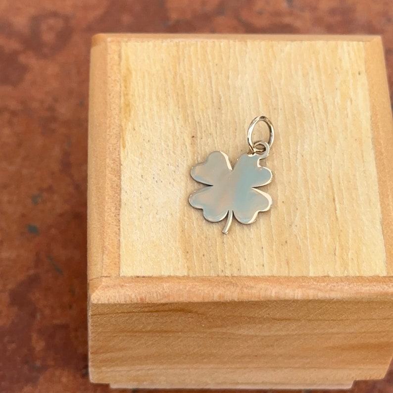 Puede incluir: Un colgante de tr&eacute;bol de cuatro hojas de oro en una caja de madera.