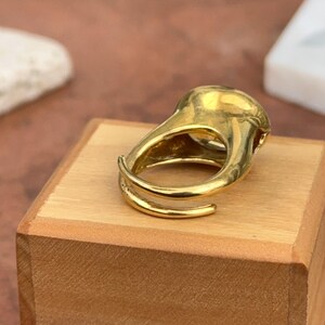 May include: A gold-colored ring with a unique, abstract design. The ring is made of metal and has a smooth, polished finish.