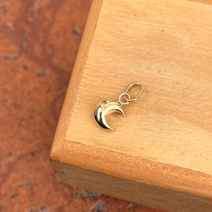 May include: A gold crescent moon charm pendant. The charm is small and delicate, with a smooth, polished finish.