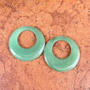 May include: Two green jade stone donut shaped pendants with a hole in the center.