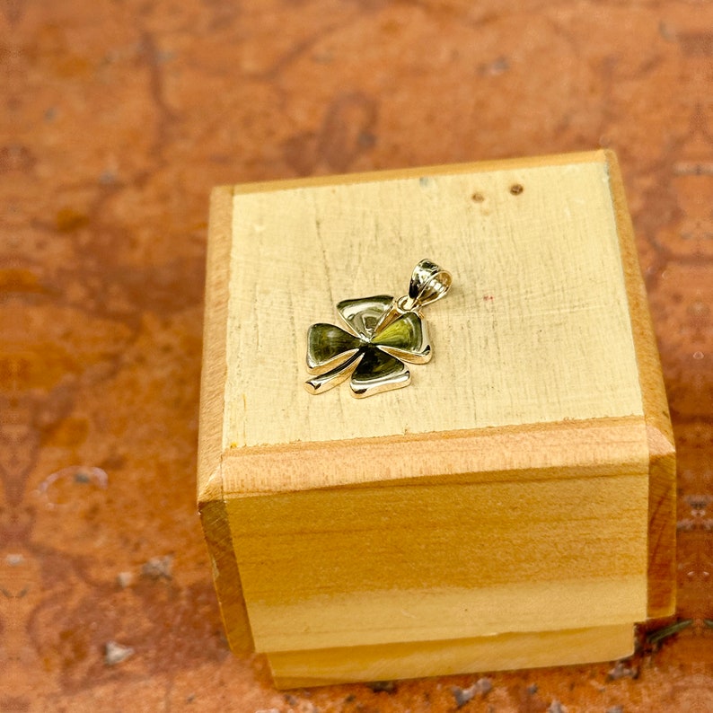 May include: A gold four-leaf clover charm pendant displayed on a wooden box.