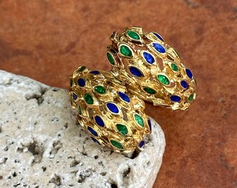 May include: A pair of gold-toned earrings with a textured design. Each earring features a pattern of green and blue oval-shaped accents. The earrings are displayed on a light-colored, textured surface.