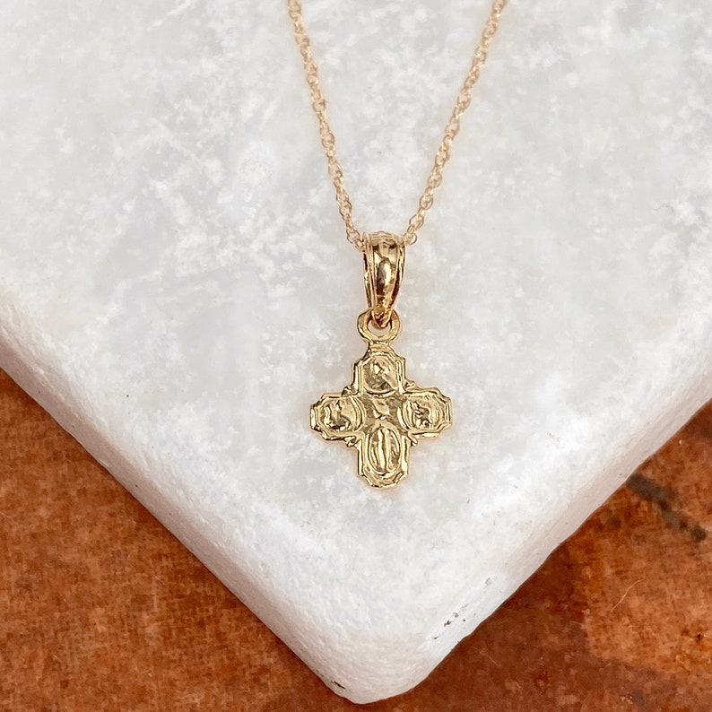 Op de afbeelding: Een gouden ketting met een klein, gedetailleerd kruisje als hanger. Het kruis heeft een getextureerd oppervlak en is een populair religieus symbool.