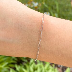 Pu&ograve; includere: Un braccialetto a catena d'argento con un design delicato e collegato. Il braccialetto &egrave; mostrato sul polso di una persona.