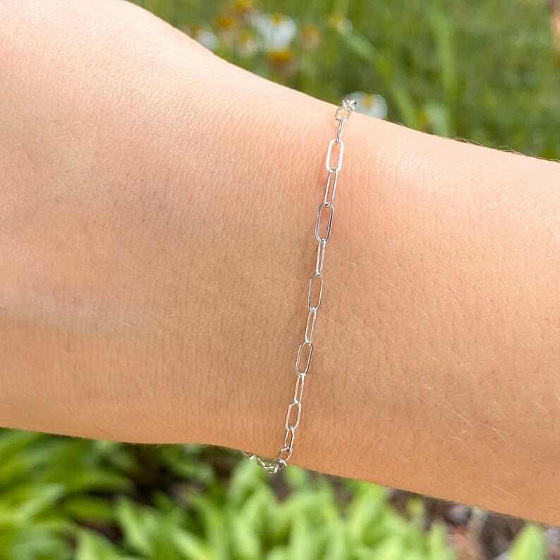 Pu&ograve; includere: Un braccialetto a catena d'argento con un design delicato e collegato. Il braccialetto &egrave; mostrato sul polso di una persona.