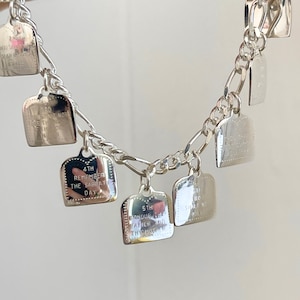 May include: A silver charm bracelet with multiple charms featuring the Ten Commandments. Each charm is shaped like a small bread loaf and has a different commandment inscribed on it.