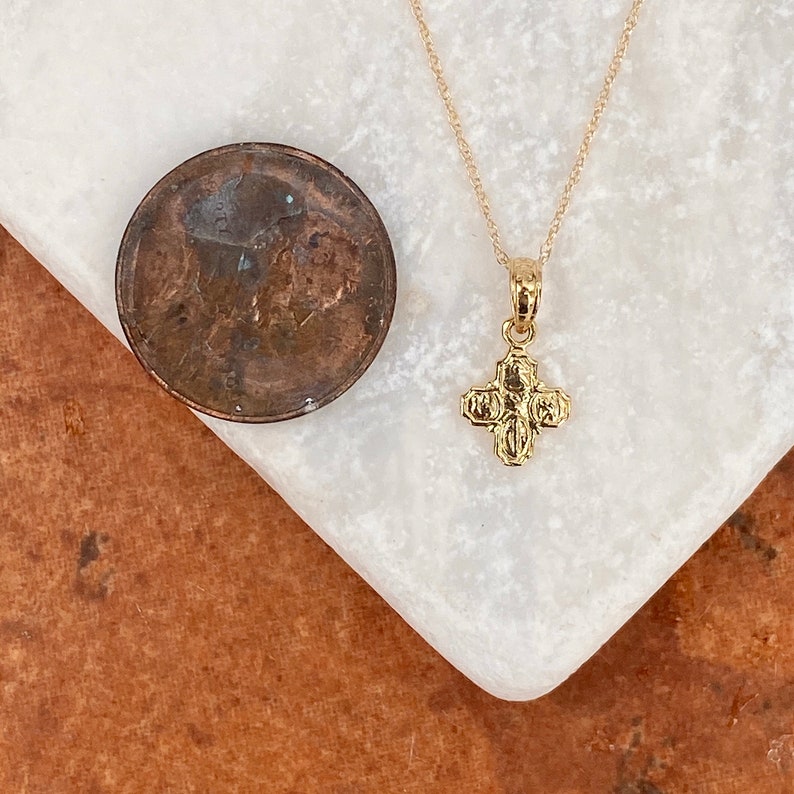 Op de afbeelding: Een gouden ketting met een klein, gedetailleerd kruisje als hanger. De hanger is ongeveer zo groot als een Nederlandse cent.