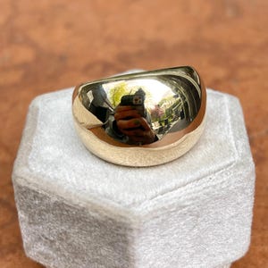 May include: A large, silver, dome-shaped ring. The ring is smooth and polished, reflecting the surrounding environment.