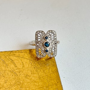 May include: A silver ring with a rectangular, filigree design featuring three blue sapphires and smaller white diamonds.
