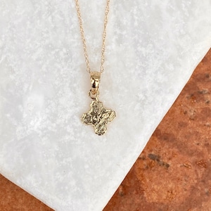 Op de afbeelding: Een gouden ketting met een klein, getextureerd kruisje als hanger. Het kruis heeft de inscriptie "IKKE" erop.
