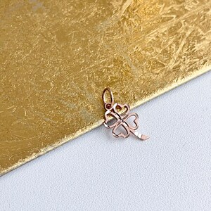 May include: A gold-toned four-leaf clover charm pendant. The pendant is made of metal and has a delicate, intricate design.