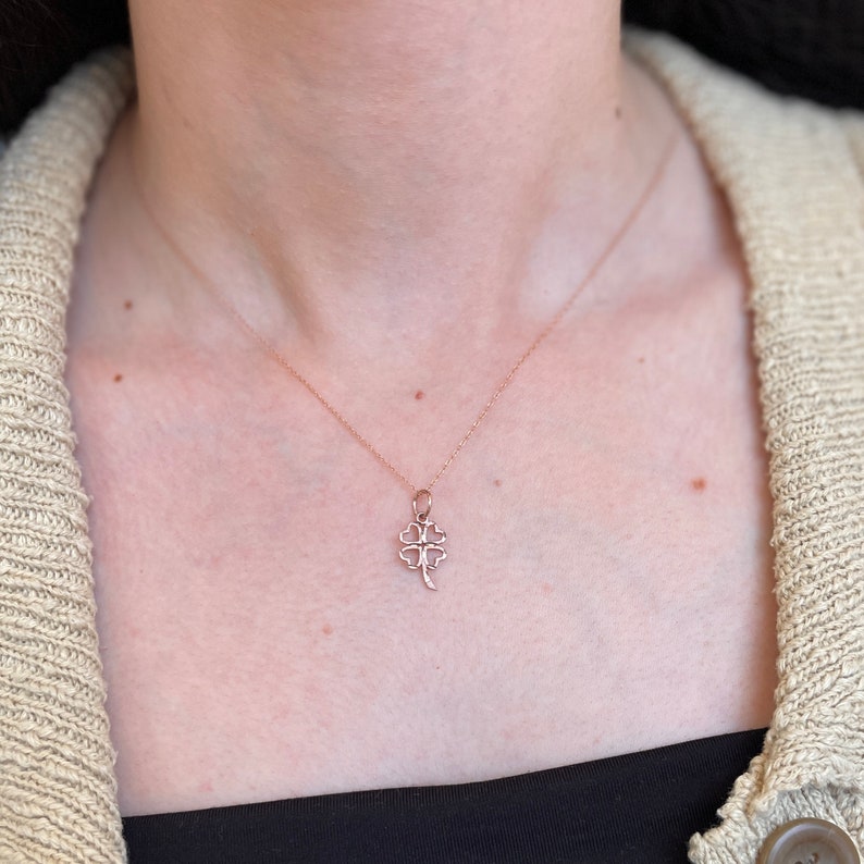 May include: A delicate rose gold necklace with a four-leaf clover pendant. The pendant is a simple, open design with a slightly curved stem.